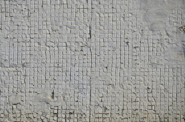 The texture of the old concrete wall, with a coating of shallow tiles of square shape, painted in gray. Background image of a wall of many square white tiles