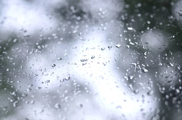 Çiçek açması yeşil ağaçların bulanık manzaralı pencere camına bir fotoğraf yağmur bırakır. Soyut resim bulutlu ve yağmurlu hava koşulları gösterilen