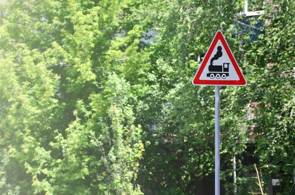 Triangular road sign with a picture of a black locomotive on a white background in a red frame. Warning sign for the presence of a railway crossing the motor road