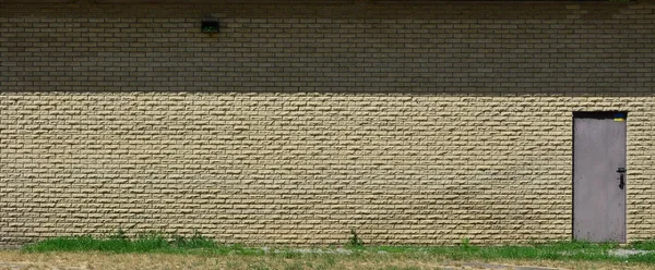 Texture of brick wall from relief stones under bright sunlight with metal door