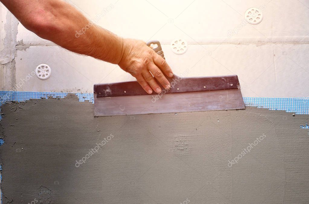 Hands of an old manual worker with wall plastering tools renovating house. Plasterer renovating outdoor walls and corners with spatula and plaster. Wall insulation. Construction finishing works