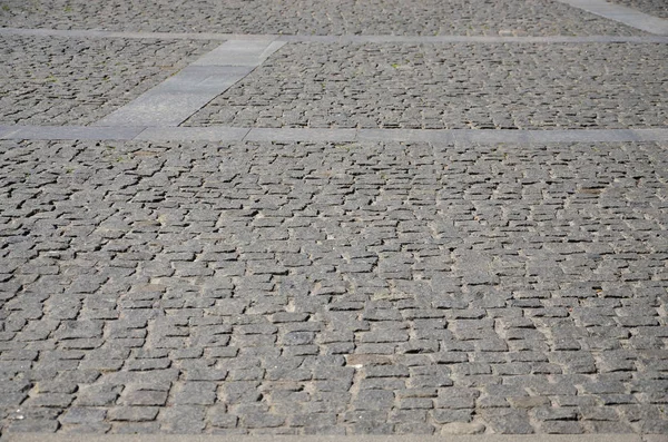 The texture of the paving slab (paving stones) of many small stones of a square shape under bright sunlight