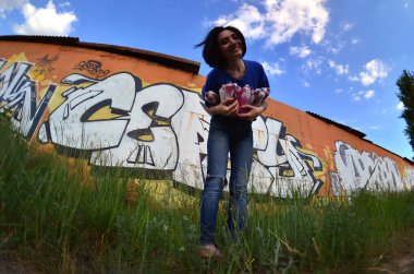 Siyah saçlı ve piercing ile duygusal bir genç kız portresi. Sprey boya... kutularını graffiti duvar arka plan üzerinde elinde bir kızla bir geniş açı fotoğraf. Bir balıkgözü lens modern bir portresi