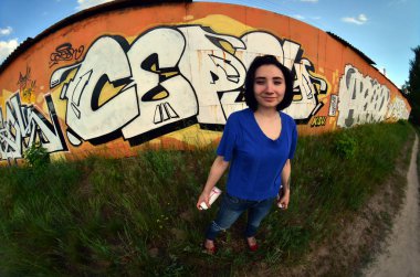 Siyah saçlı ve piercing ile duygusal bir genç kız portresi. Sprey boya... kutularını graffiti duvar arka plan üzerinde elinde bir kızla bir geniş açı fotoğraf. Bir balıkgözü lens modern bir portresi