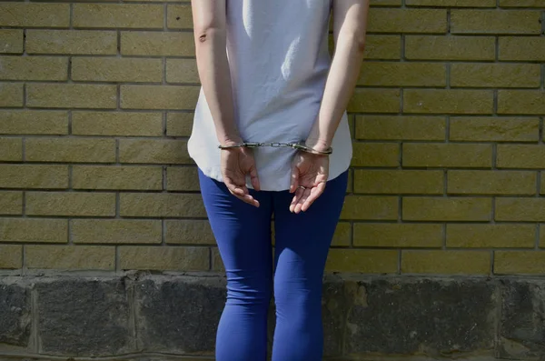 一个年轻的犯罪女孩的身体碎片与手在一个黄色的砖墙背景手铐 城市环境中女性犯罪嫌疑人的羁押理念 — 图库照片