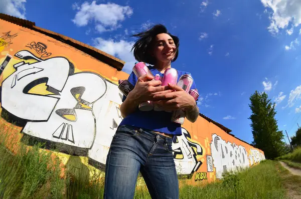 Siyah saçlı ve piercing ile duygusal bir genç kız portresi. Sprey boya... kutularını graffiti duvar arka plan üzerinde elinde bir kızla bir geniş açı fotoğraf. Bir balıkgözü lens modern bir portresi
