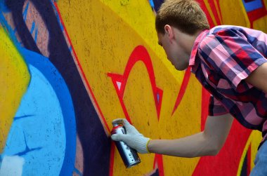 Bir genç Kızıl saçlı grafiti sanatçısı yeni bir graffiti duvar boyar. Bir duvara yakın çekim bir grafiti çizim işlemi fotoğrafı. Sokak sanatı ve yasadışı vandalizm kavramı