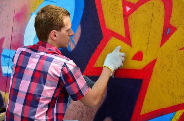 Bir genç Kızıl saçlı grafiti sanatçısı yeni bir graffiti duvar boyar. Bir duvara yakın çekim bir grafiti çizim işlemi fotoğrafı. Sokak sanatı ve yasadışı vandalizm kavramı