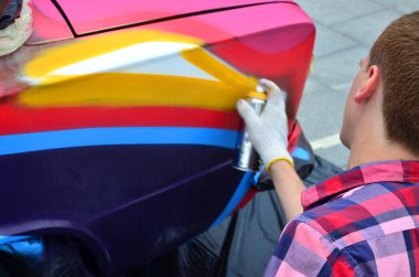 Bir genç Kızıl saçlı grafiti sanatçısı araba yeni bir renkli grafiti boyar. Bir araba yakın çekim bir grafiti çizim işlemi fotoğrafı. Sokak sanatı ve yasadışı vandalizm kavramı