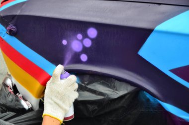 Bir el bir sprey ile yeni bir renkli grafiti arabanın üzerine çekiyor olabilir. Otomobil bir yakın çekim bir grafiti çizim işlemi fotoğrafı. Sokak sanatı ve yasadışı vandalizm kavramı