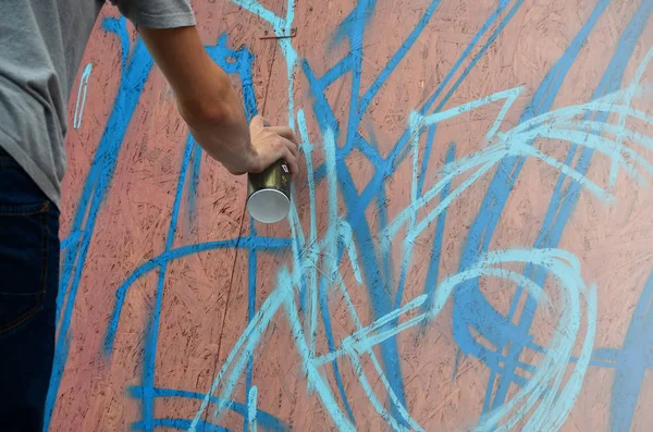 A hand with a spray can that draws a new graffiti on the wall. Photo of the process of drawing a graffiti on a wooden wall close-up. The concept of street art and illegal vandalism