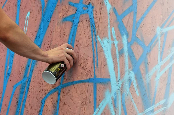 A hand with a spray can that draws a new graffiti on the wall. Photo of the process of drawing a graffiti on a wooden wall close-up. The concept of street art and illegal vandalism