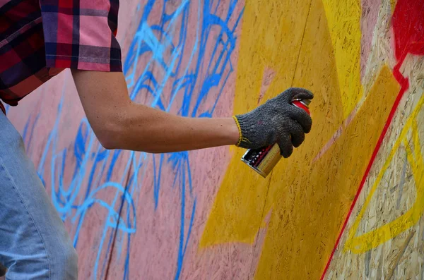 A hand with a spray can that draws a new graffiti on the wall. Photo of the process of drawing a graffiti on a wooden wall close-up. The concept of street art and illegal vandalism