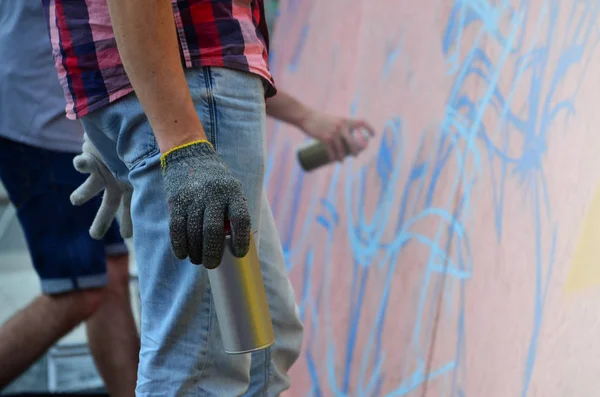 A hand with a spray can that draws a new graffiti on the wall. Photo of the process of drawing a graffiti on a wooden wall close-up. The concept of street art and illegal vandalism