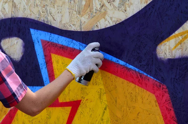 A hand with a spray can that draws a new graffiti on the wall. Photo of the process of drawing a graffiti on a wooden wall close-up. The concept of street art and illegal vandalism