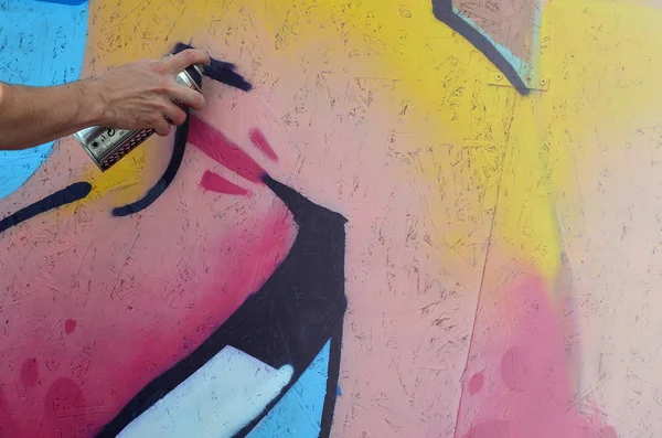 A hand with a spray can that draws a new graffiti on the wall. Photo of the process of drawing a graffiti on a wooden wall close-up. The concept of street art and illegal vandalism