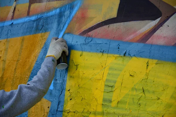 A hand with a spray can that draws a new graffiti on the wall. Photo of the process of drawing a graffiti on a concrete wall close-up. The concept of street art and illegal vandalism