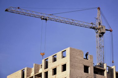 Yüksek binaların yapım aşamasında karşı açık mavi gökyüzü ile yer içinde çalışan uzun boylu vinç. Vinç ve çalışma ilerleme boşaltmak ile bina