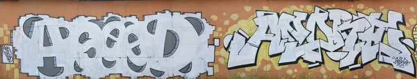 A photo of several graffiti artworks on the metal wall. Graffiti drawings are made with white paint with black outlines and have an orange background. Texture of wall with graffiti decoration