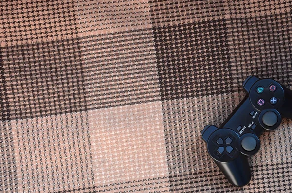 市松模様のファブリックのカバーの背景に黒プラスチック製ワイヤレス ゲーム コント ローラーのクローズ アップ写真 ゲームのジョイスティック ビデオ ゲームをプレイに行こう — ストック写真