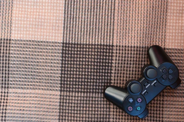 The video game controller from the game console is on the checkered sofa. Wireless device for controlling during video games