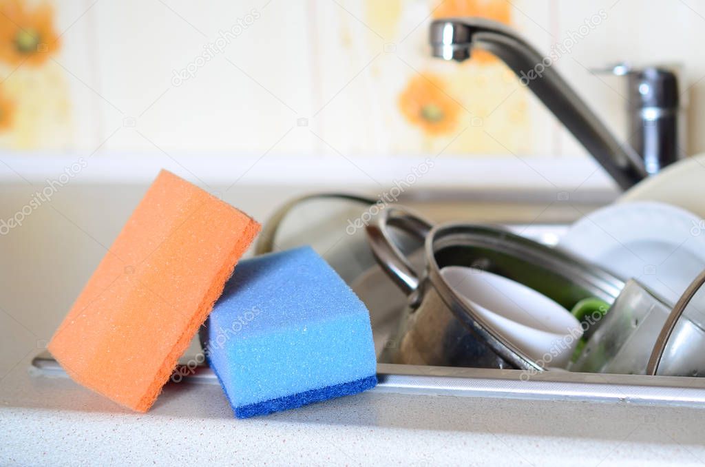 A few sponges lie on the background of the sink with dirty dishes