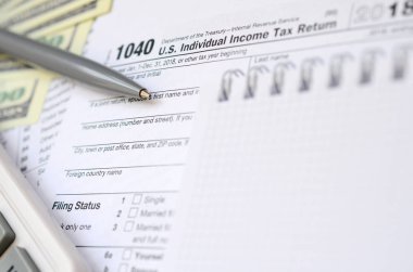 Kalem, defter, hesap makinesi ve dolar faturaları yalanlar üzerine vergi 1040 ABD bireysel gelir vergisi beyannamesi formu var. Vergi ödemek için zaman