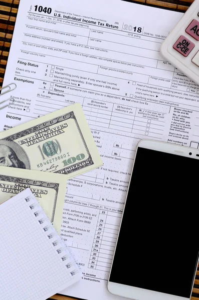 Composition of items lying on the 1040 tax form. Dollar bills, calculator, smartphone, paper clip and notepad. The time to pay taxes