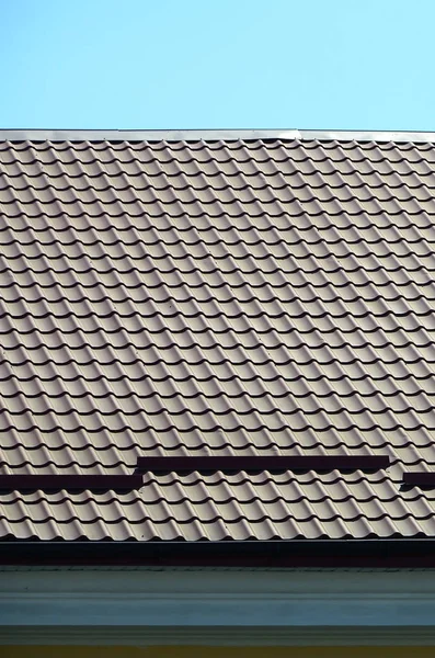 A fragment of a roof from a metal tile of dark red color. Quality Roofing