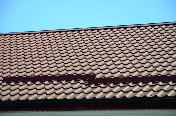 A fragment of a roof from a metal tile of dark red color. Quality Roofing