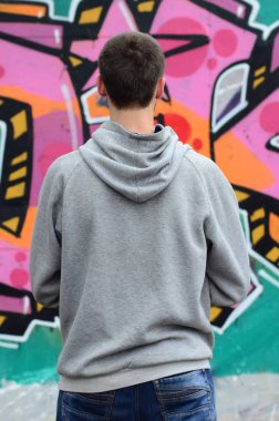 Gri kapüşonlu bir genç grafiti sanatçısı bir duvara yağmurlu havalarda pembe ve yeşil renklerde onun graffiti ile duvara görünüyor. Sokak sanatı kavramı