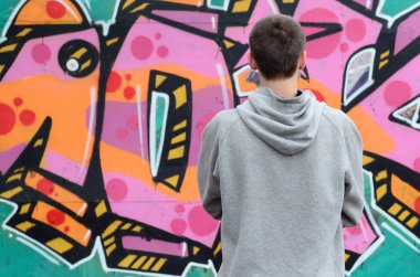 Gri kapüşonlu bir genç grafiti sanatçısı bir duvara yağmurlu havalarda pembe ve yeşil renklerde onun graffiti ile duvara görünüyor. Sokak sanatı kavramı