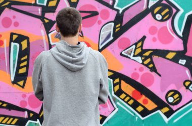 Gri kapüşonlu bir genç grafiti sanatçısı bir duvara yağmurlu havalarda pembe ve yeşil renklerde onun graffiti ile duvara görünüyor. Sokak sanatı kavramı