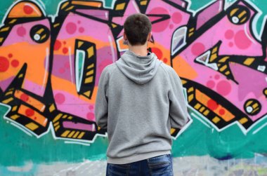 Gri kapüşonlu bir genç grafiti sanatçısı bir duvara yağmurlu havalarda pembe ve yeşil renklerde onun graffiti ile duvara görünüyor. Sokak sanatı kavramı