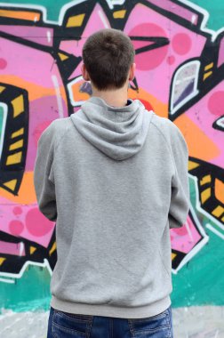Gri kapüşonlu bir genç grafiti sanatçısı bir duvara yağmurlu havalarda pembe ve yeşil renklerde onun graffiti ile duvara görünüyor. Sokak sanatı kavramı