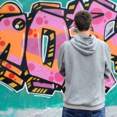 Gri kapüşonlu bir genç grafiti sanatçısı bir duvara yağmurlu havalarda pembe ve yeşil renklerde onun graffiti ile duvara görünüyor. Sokak sanatı kavramı