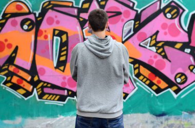 Gri kapüşonlu bir genç grafiti sanatçısı bir duvara yağmurlu havalarda pembe ve yeşil renklerde onun graffiti ile duvara görünüyor. Sokak sanatı kavramı