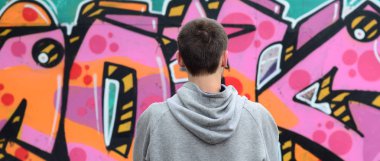 Gri kapüşonlu bir genç grafiti sanatçısı bir duvara yağmurlu havalarda pembe ve yeşil renklerde onun graffiti ile duvara görünüyor. Sokak sanatı kavramı