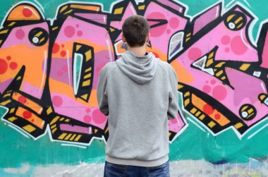 Gri kapüşonlu bir genç grafiti sanatçısı bir duvara yağmurlu havalarda pembe ve yeşil renklerde onun graffiti ile duvara görünüyor. Sokak sanatı kavramı