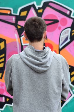 Gri kapüşonlu bir genç grafiti sanatçısı bir duvara yağmurlu havalarda pembe ve yeşil renklerde onun graffiti ile duvara görünüyor. Sokak sanatı kavramı