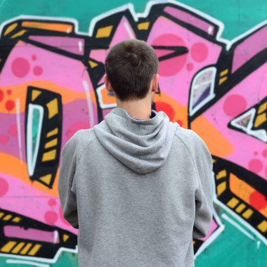 Gri kapüşonlu bir genç grafiti sanatçısı bir duvara yağmurlu havalarda pembe ve yeşil renklerde onun graffiti ile duvara görünüyor. Sokak sanatı kavramı