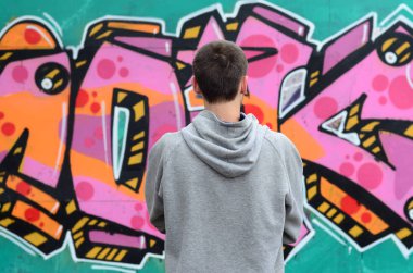 Gri kapüşonlu bir genç grafiti sanatçısı bir duvara yağmurlu havalarda pembe ve yeşil renklerde onun graffiti ile duvara görünüyor. Sokak sanatı kavramı