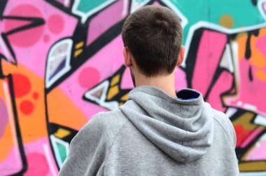 Gri kapüşonlu bir genç grafiti sanatçısı bir duvara yağmurlu havalarda pembe ve yeşil renklerde onun graffiti ile duvara görünüyor. Sokak sanatı kavramı