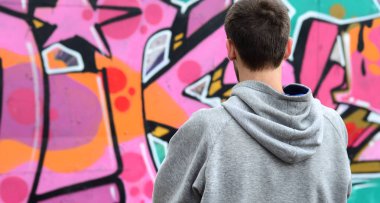 Gri kapüşonlu bir genç grafiti sanatçısı bir duvara yağmurlu havalarda pembe ve yeşil renklerde onun graffiti ile duvara görünüyor. Sokak sanatı kavramı