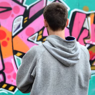 Gri kapüşonlu bir genç grafiti sanatçısı bir duvara yağmurlu havalarda pembe ve yeşil renklerde onun graffiti ile duvara görünüyor. Sokak sanatı kavramı