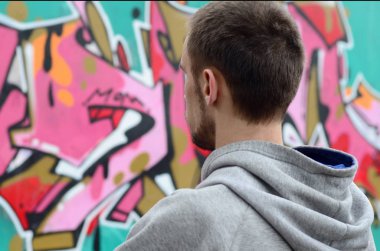 Gri kapüşonlu bir genç grafiti sanatçısı bir duvara yağmurlu havalarda pembe ve yeşil renklerde onun graffiti ile duvara görünüyor. Sokak sanatı kavramı