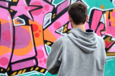 Gri kapüşonlu bir genç grafiti sanatçısı bir duvara yağmurlu havalarda pembe ve yeşil renklerde onun graffiti ile duvara görünüyor. Sokak sanatı kavramı