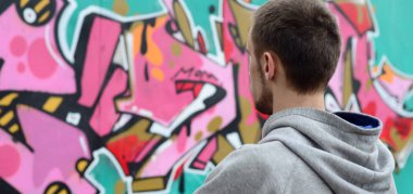 Gri kapüşonlu bir genç grafiti sanatçısı bir duvara yağmurlu havalarda pembe ve yeşil renklerde onun graffiti ile duvara görünüyor. Sokak sanatı kavramı