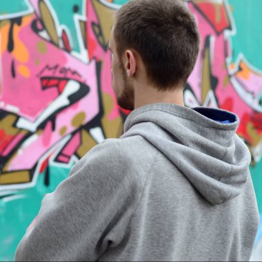 Gri kapüşonlu bir genç grafiti sanatçısı bir duvara yağmurlu havalarda pembe ve yeşil renklerde onun graffiti ile duvara görünüyor. Sokak sanatı kavramı