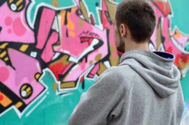 Gri kapüşonlu bir genç grafiti sanatçısı bir duvara yağmurlu havalarda pembe ve yeşil renklerde onun graffiti ile duvara görünüyor. Sokak sanatı kavramı